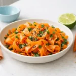 Carrot ribbon salad in a shallow bowl with soy-lime-sesame dressing, parsley, and toasted sesame seeds