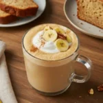 Banana bread latte in a clear glass mug topped with whipped cream, banana chips, and chopped nuts.