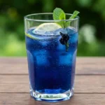 Glass of butterfly pea lemonade on a wooden table with lemon and mint garnish