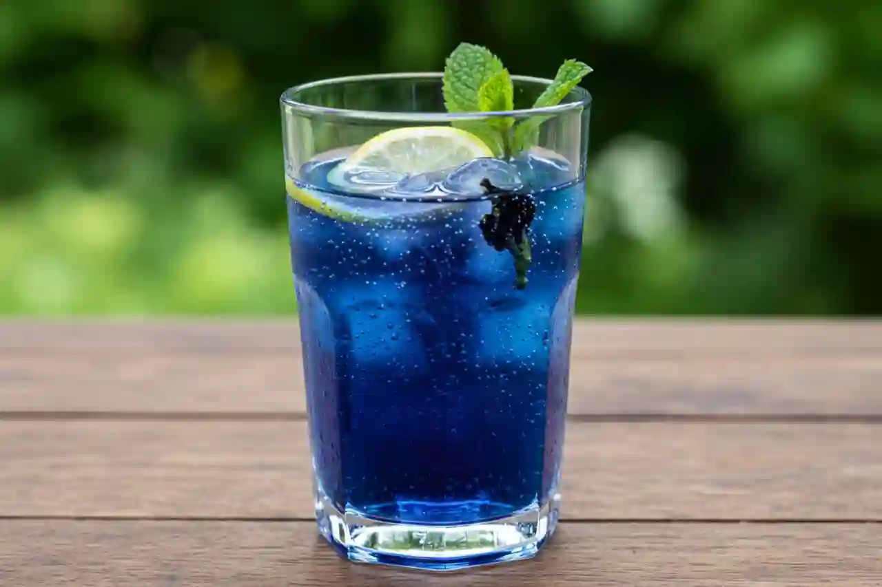 Glass of butterfly pea lemonade on a wooden table with lemon and mint garnish