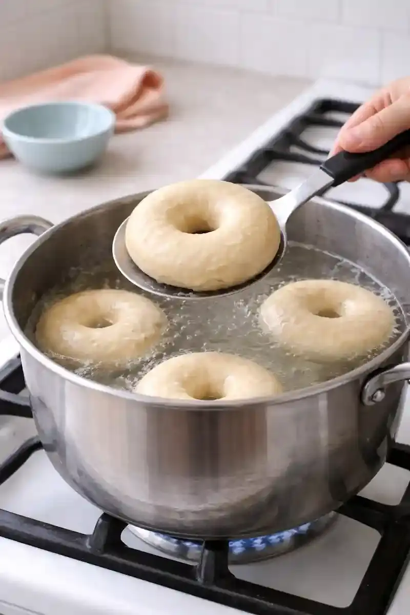 Boiling Bagels Before Baking Homemade bagels boiling in a pot of water before baking in a bright kitchen
