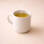 A steaming cup of green tea in a white mug on a clean countertop.
