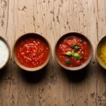 Top-down view of four homemade sauces in ceramic bowls on a rustic wooden counter